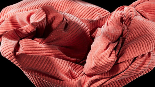 Pink corduroy fabric is gently ruffled and folded.